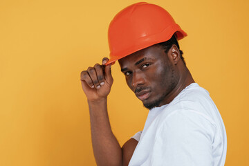 Wall Mural - In orange hard hat. Construction worker. Handsome black man is in the studio against yellow background
