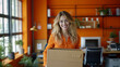 Young white woman, blonde, smiling, holding a box in an orange office.