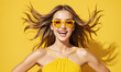 Happy smiling excited young beautiful woman in yellow summer dress on yellow studio background