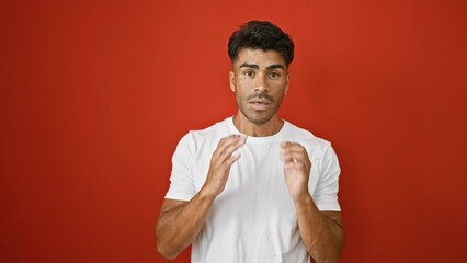 Wall Mural - A handsome young hispanic man with a beard poses against an isolated red wall, expressing varied emotions.