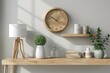 © Graph Squad - A simple wooden clock on the wall above an empty white desk, with a modern minimalist lamp and potted plant beside it.
