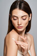 © LIGHTFIELD STUDIOS - A young Caucasian woman with brunette hair gracefully applying cream on shoulder