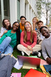 © CarlosBarquero - Vertical Portrait of a large group multiracial friends sitting posing smiling with laptop and workbooks looking to camera outdoor. Happy young classmates together outside university campus building