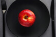 Red apple on a black plate next to utensils