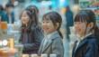 © Surachetsh - Joyful Asian Japanese kids in business attire chat and laugh by an exhibition booth, with tables of products and milk cups in the background.