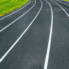 Wall Mural - Track and Field Running Lanes. Overhead view of a rubber black running track surface with slightly curved white lane lines. Natural grass surface on the inside of the circular track.