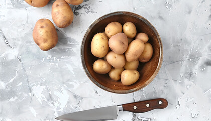 Bowl with raw potatoes and knife on light background