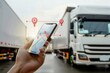 © Georgii - Close-up of a hand holding a smartphone with a GPS tracking app against trucks