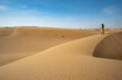 Frau in gelbem Kleid steht auf einer Sanddüne, blickt in die Wüste Namib
