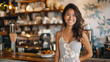 A warmly decorated coffee shop featuring a businesswoman wearing a stylish summer dress grinning broadly at the camera.
