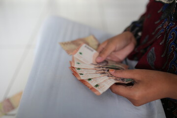 A woman's hand holds five thousand Indonesian notes for the Eid al-Fitr holiday