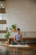 © Jovo Jovanovic/Stocksy - Calm woman meditating on yoga mat against wall at home