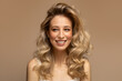A young blonde woman with curly beautiful hair smiles on a beige background.