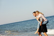 © peopleimages.com - Couple, ocean waves and piggyback on vacation, smile and peace at beach or game by blue sky. People, happy and tropical island for bonding on weekend, outdoor nature and love for marriage or romance
