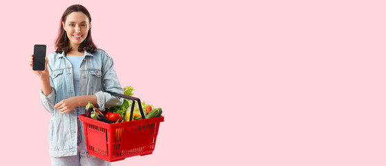 Canvas Print - Young woman with shopping basket of fresh vegetables and mobile phone on pink background