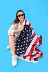 Wall Mural - Young woman with USA flag sitting on blue background