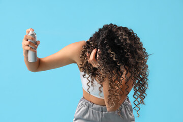 Wall Mural - Beautiful African-American woman spraying hair on blue background