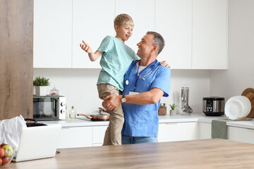 Poster - Mature doctor holding his little son in kitchen