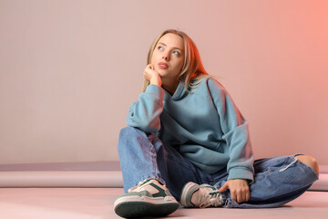 Poster - Stylish young woman in jeans sitting on light background