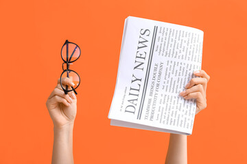 Female hands with newspaper and eyeglasses on orange background