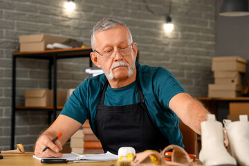 Sticker - Mature shoemaker writing at table in workshop