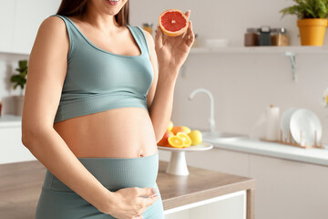 Wall Mural - Sporty pregnant woman with grapefruit in kitchen, closeup