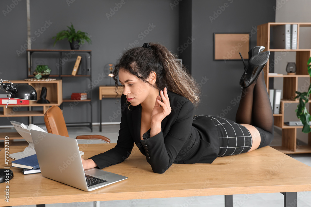 Attractive African-American secretary working with laptop on table in office