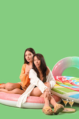 Sticker - Female Asian friends sitting on swim ring against green background