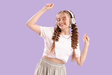 Canvas Print - Happy smiling young woman with braids in headphones dancing on lilac background