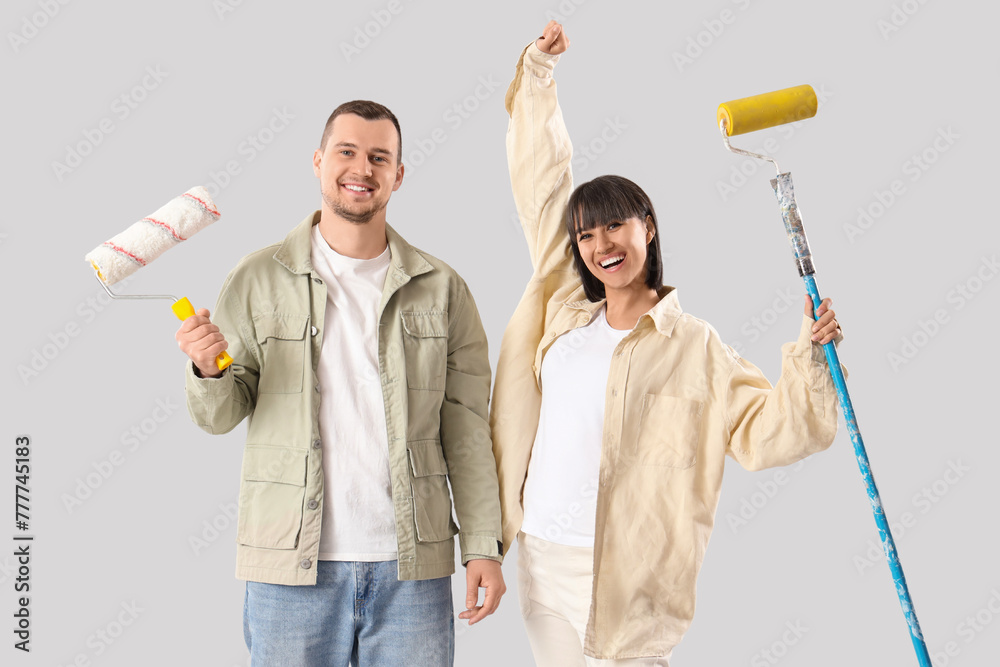 Young couple with paint rollers on light background. Repair concept