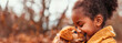 Young black girl child gently holding a small puppy in her arms, both looking towards camera with a sense of innocence and joy. Friendship with a pet. Banner. Copy space