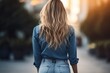 Urban elegance captured-a long-haired blonde in jeans, viewed from behind, poses against the vibrant cityscape, exuding style.