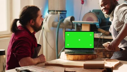 Upbeat men using CAD software on isolated screen laptop, debating wood design to use. Smiling cabinetmakers chatting, using program on chroma key notebook to make furniture schematics, camera A