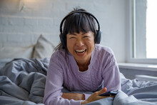Asian Woman Enjoying Music In Bed