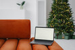 © Alina Hvostikova/Stocksy - Opened laptop placed against decorated Christmas on sofa at home