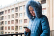 © Ibai Acevedo/Stocksy - Woman using phone with winter coat at home terrace