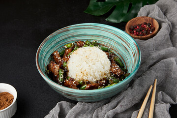 Poster - Asian food - boiled rice with fried beef and green beans in ceramic bowl on black stone background. Stir-fried beef with string beans and rice in modern style. Asian food menu in dark backdrop.