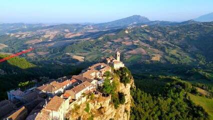 Wall Mural - Amazing aerial pedestal up unveiling fly-over of Montefalcone Appennino (Fermo) soaring in the sky to capture a supreme rocky cliff with buildings and belltower standing out on a precipice over hills