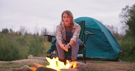 Poster - Fire, woman and camping wood with flames for heating hands and eco holiday in nature with a tent. Adventure, field and rocks in a campsite with smoke, burning and pit with travel and relax in a park