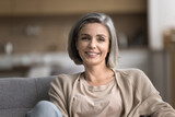 Fototapeta Tulipany - Close up portrait of smiling mature woman looking at camera, pose for photo, relax on cozy couch in living room, feels carefree on weekend alone indoors, pleasant happy lady enjoy leisure time at home