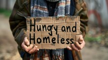 A Homeless Person Holding A Sign That Reads "Hungry And Homeless", Drawing Attention To The Interconnected Challenges Faced By Those Living In Poverty.