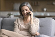 © fizkes - Carefree attractive middle-aged woman spend time on sofa in living room, hold smartphone, make call, lead pleasant conversation with friend or family enjoy remote communication using mobile connection