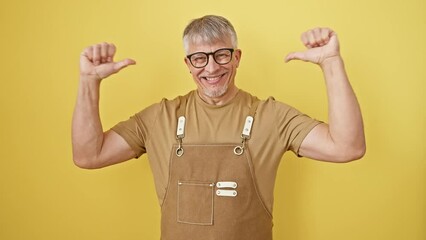 Poster - Confident grey-haired middle-aged man, happily pointing at self with a proud smile, donning glasses and apron while standing isolated on a vibrant yellow background.