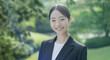 © tenpadasi - 朝のオフィス・オフィス街の公園笑顔の日本人女性会社員ポートレート　ビジネス・仕事・新入社員・若者　太陽の光　レンズフレアとゴースト　緑の前ボケ