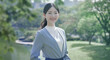 © tenpadasi - 朝のオフィス・オフィス街の公園笑顔の日本人女性会社員ポートレート　ビジネス・仕事・新入社員・若者　太陽の光　レンズフレアとゴースト　緑の前ボケ