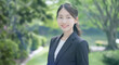 © tenpadasi - 朝のオフィス・オフィス街の公園笑顔の日本人女性会社員ポートレート　ビジネス・仕事・新入社員・若者　太陽の光　レンズフレアとゴースト　緑の前ボケ