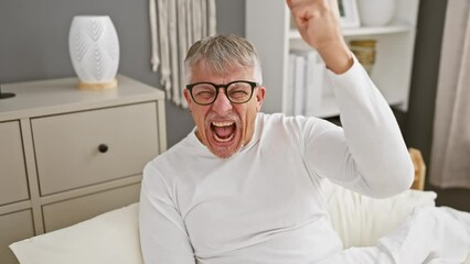 Wall Mural - Furious, aggressive middle-aged grey-haired man in pyjamas, frantic with anger, raises fist in bedroom