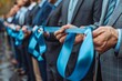 © DKPhoto - Rows of formally dressed men holding vibrant blue ribbons at an outdoor ceremony or event