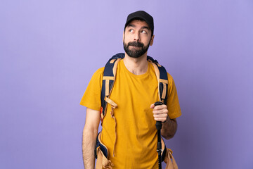 Caucasian handsome man with backpack and trekking poles over isolated background having doubts while looking up