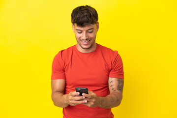 Sticker - Young caucasian handsome man isolated on yellow background sending a message with the mobile